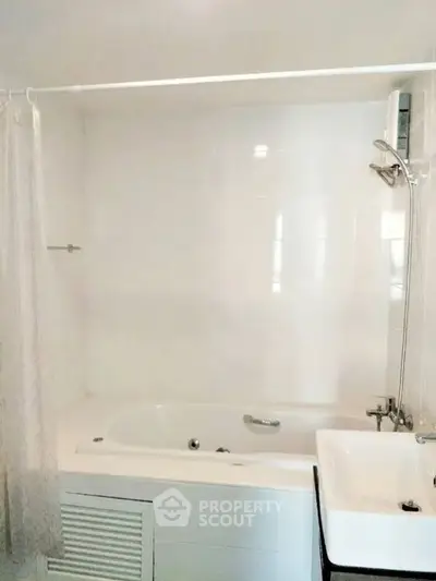 Modern bathroom with bathtub and shower, featuring sleek white tiles and a compact sink.