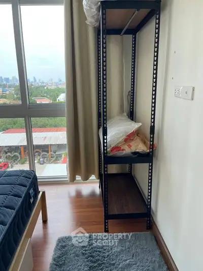 Cozy bedroom with city view, featuring a bed, shelf, and plush rug, ideal for urban living.