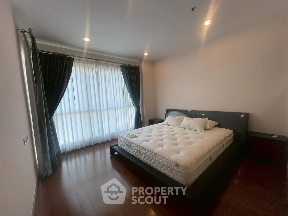 Spacious bedroom with large window and elegant curtains, featuring a comfortable bed and wooden flooring.