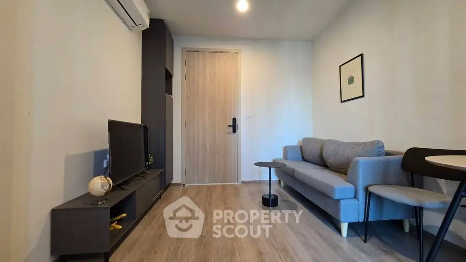 Modern living room with sleek furniture and wooden flooring, featuring a cozy sofa and wall-mounted TV.