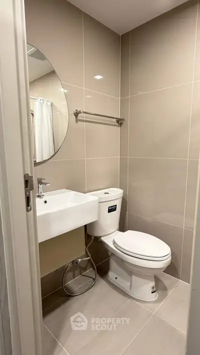Modern bathroom with sleek fixtures and neutral tiles, featuring a round mirror and compact design.
