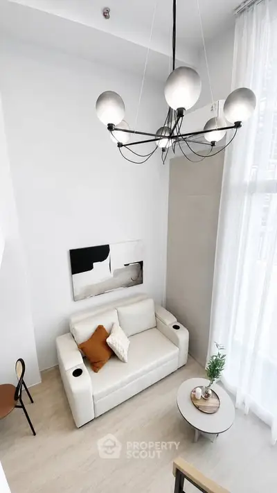Modern living room with high ceiling, elegant chandelier, and cozy white sofa in a bright, airy space.