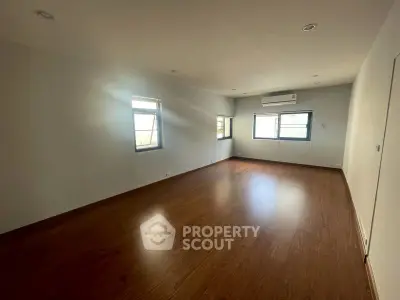 Spacious empty room with wooden flooring and large windows, perfect for customization.