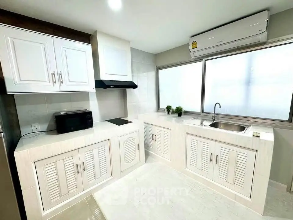 Modern kitchen with sleek white cabinetry and large window for natural light.