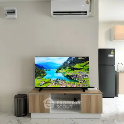 Modern living room with sleek TV setup and kitchen area, showcasing contemporary design and functionality.