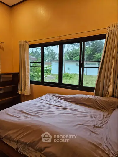 Cozy bedroom with large window offering serene garden view, perfect for relaxation and comfort.