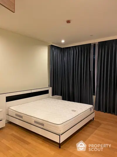 Spacious bedroom with polished hardwood floors and elegant dark curtains, featuring a large comfortable bed and modern minimalist furniture.