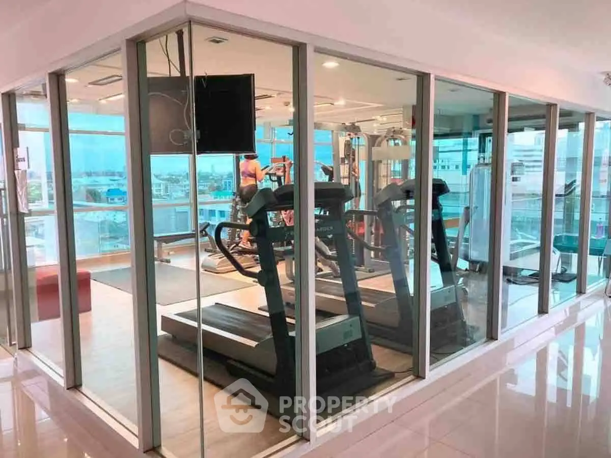 Modern gym with glass walls and city view, featuring state-of-the-art fitness equipment.
