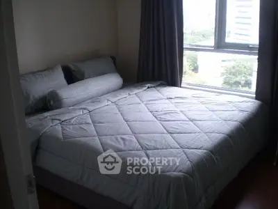 Cozy bedroom with large window and modern bedding in a high-rise apartment.