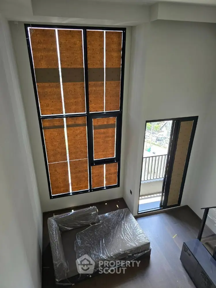 Modern duplex interior with high ceilings and large windows, featuring a partially furnished living area.