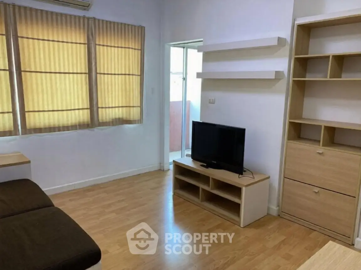 Cozy living room with wooden flooring, TV unit, and natural light from large windows.