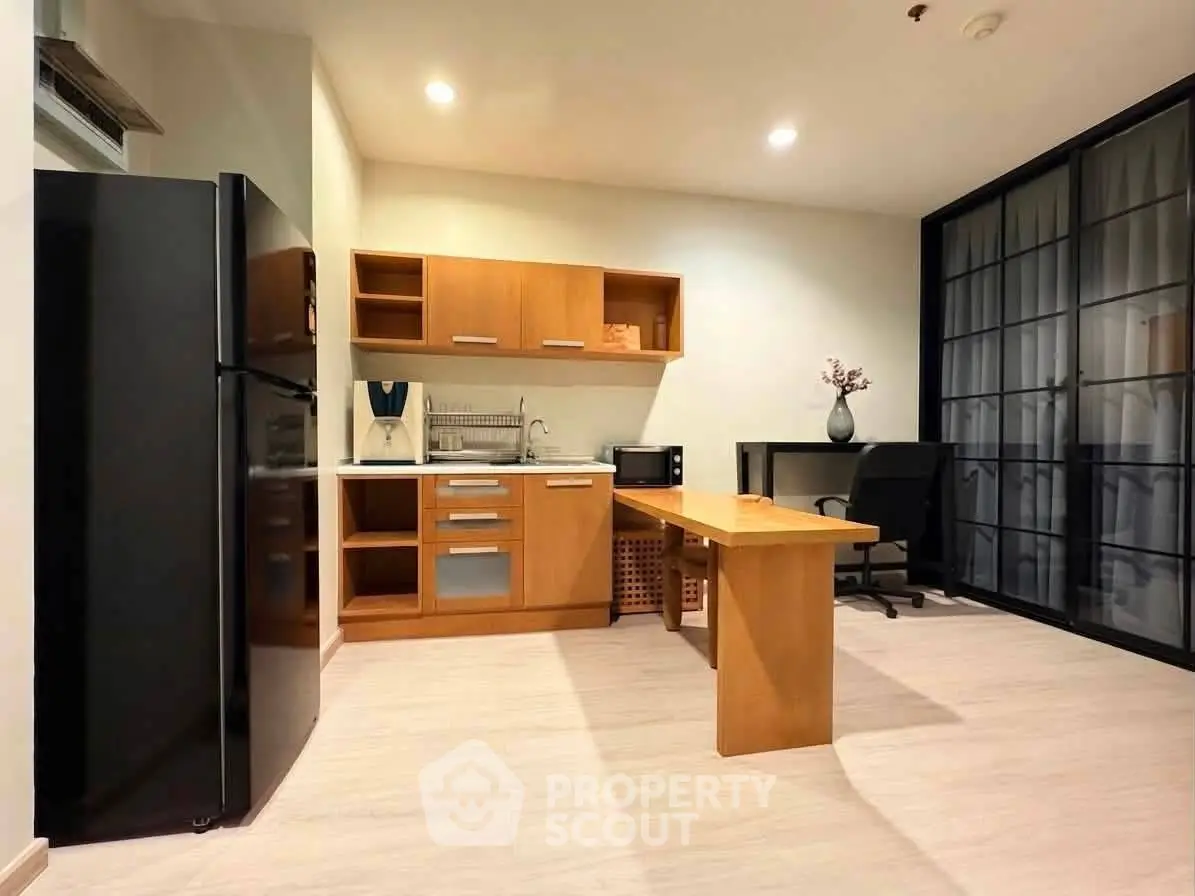 Modern kitchen with sleek black fridge and wooden cabinetry in open layout apartment.