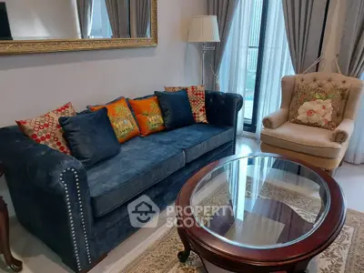 Elegant living room with plush blue sofa and armchair, featuring a glass coffee table and stylish decor.