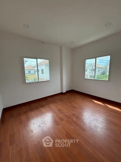 Spacious empty room with wooden flooring and large windows in a modern home.