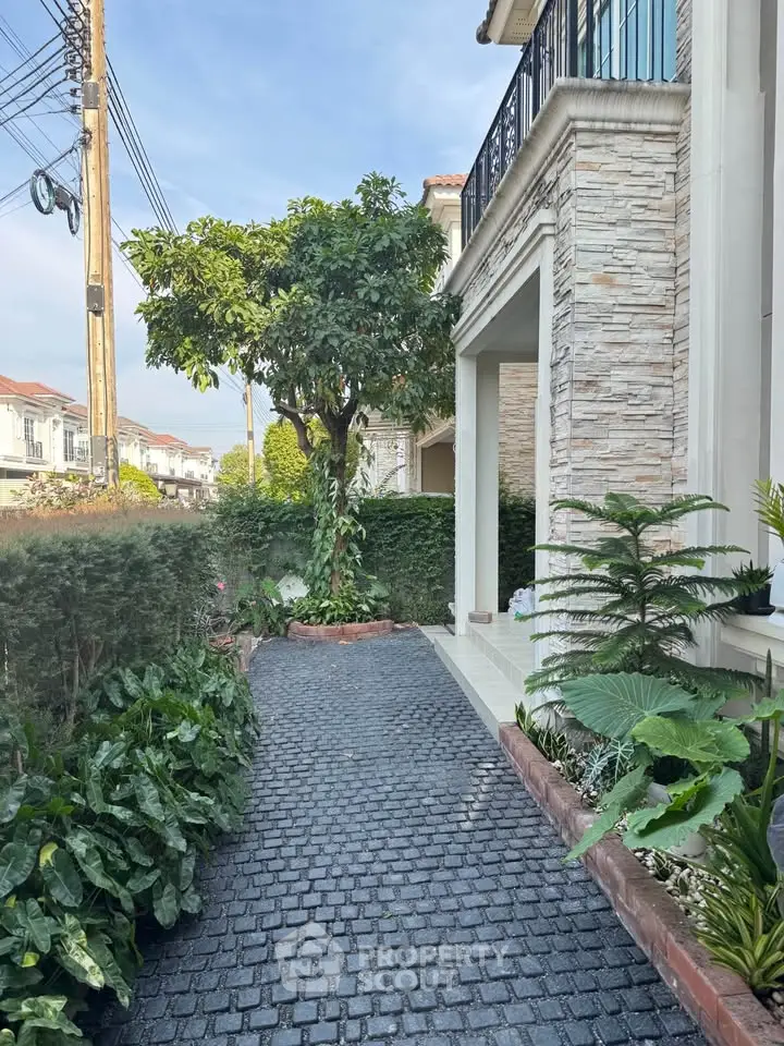 Charming garden pathway beside elegant stone facade of modern home, lush greenery enhances curb appeal.