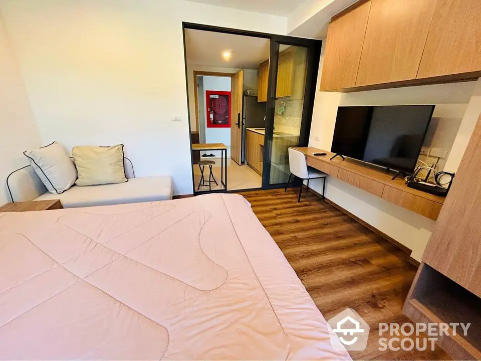 Modern bedroom with wooden flooring and built-in TV unit, adjacent to a compact kitchen.