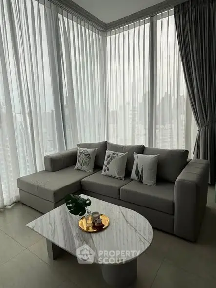 Modern living room with stylish gray sofa and marble coffee table, featuring floor-to-ceiling windows with city view.