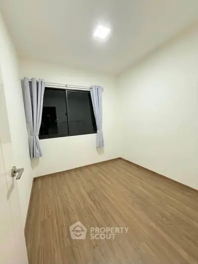 Spacious empty bedroom with wooden flooring and large window, perfect for customization.