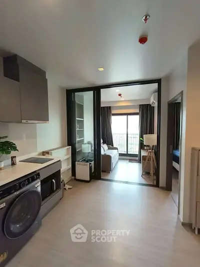 Modern apartment with open layout, featuring a sleek kitchen and spacious living area with large windows.