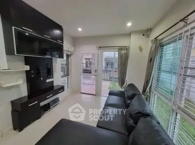 Modern living room with sleek black sofa and large windows offering ample natural light.
