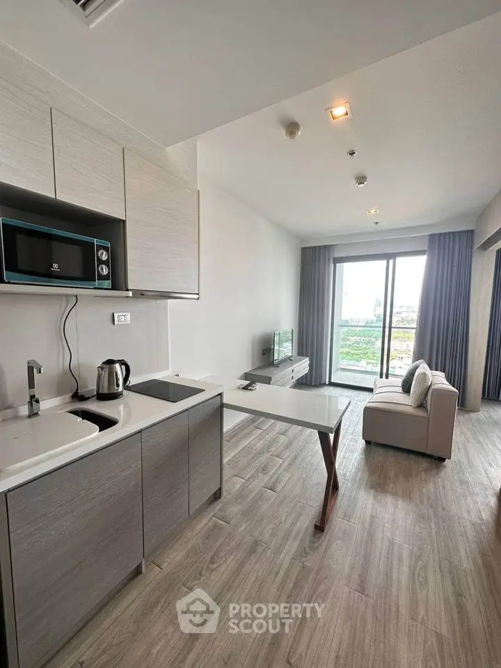 Modern open-plan living room with kitchen, featuring sleek design and large windows offering a scenic view.