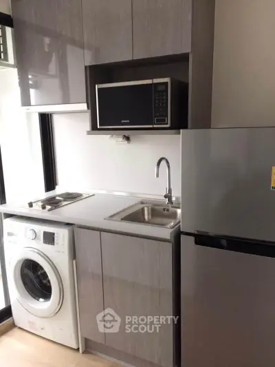 Compact modern kitchen with washing machine, microwave, and fridge in sleek design.