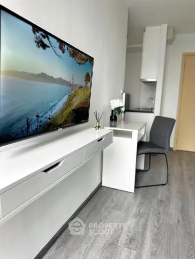 Modern studio apartment with sleek design and wall-mounted TV, featuring a compact kitchen and stylish decor.