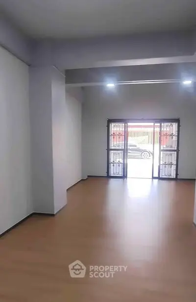 Spacious empty room with wooden flooring and large window, ideal for customization.