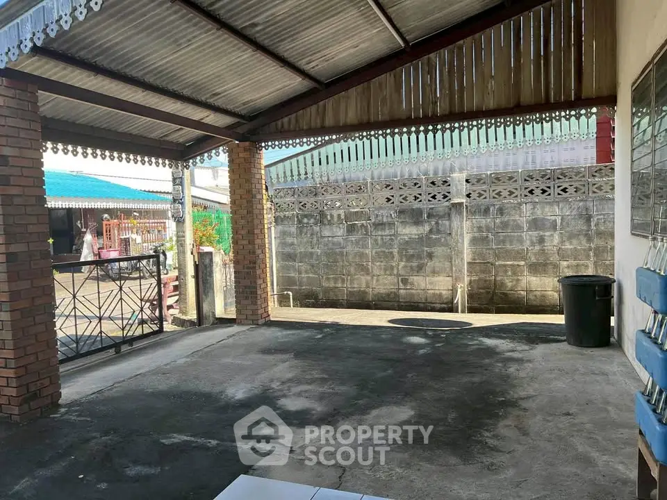 Spacious covered parking area with brick pillars and metal gate in residential property.