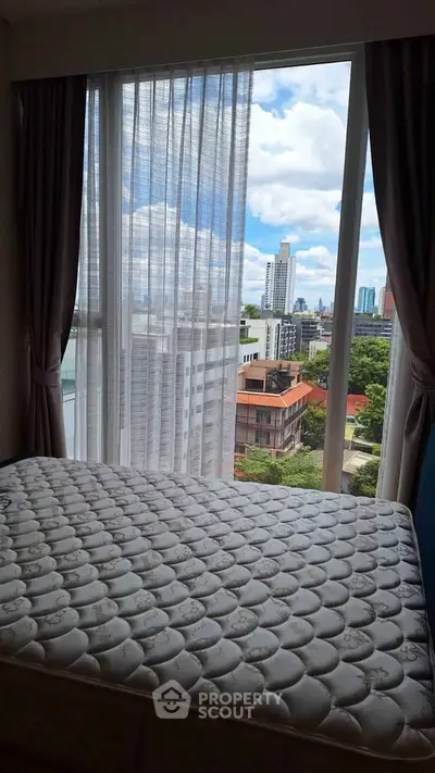 Bright bedroom with large window offering stunning city view, featuring a comfortable mattress.