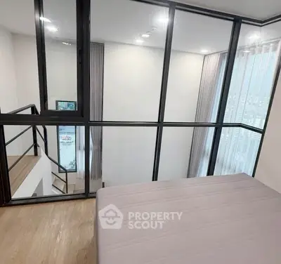 Modern loft bedroom with glass walls and wooden flooring, offering a stylish and open living space.