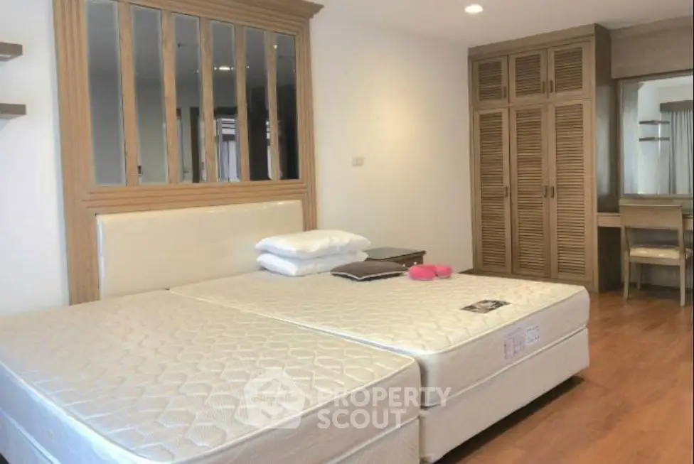 Spacious bedroom with twin beds and wooden wardrobe in modern apartment.