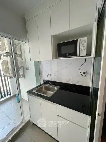 Modern compact kitchen with sleek cabinetry and microwave, featuring a balcony view.