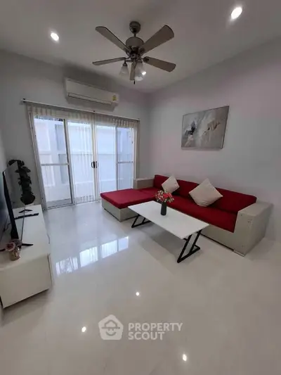 Modern living room with red sofa, ceiling fan, and large windows for natural light.