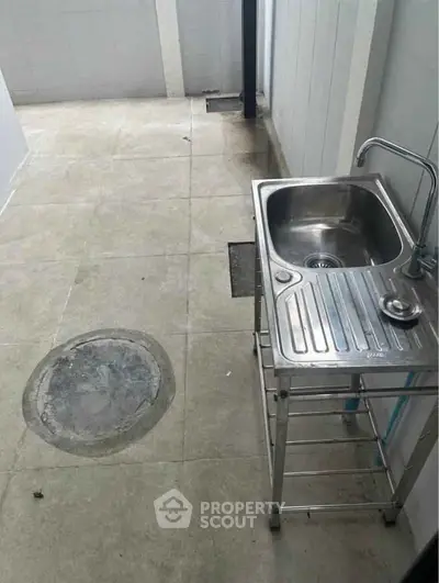 Compact utility area with stainless steel sink and tiled flooring, ideal for practical use in modern homes.