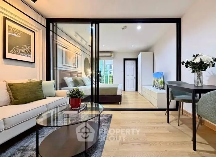 Modern open-plan living room with glass partition to bedroom, stylish decor, and natural light.