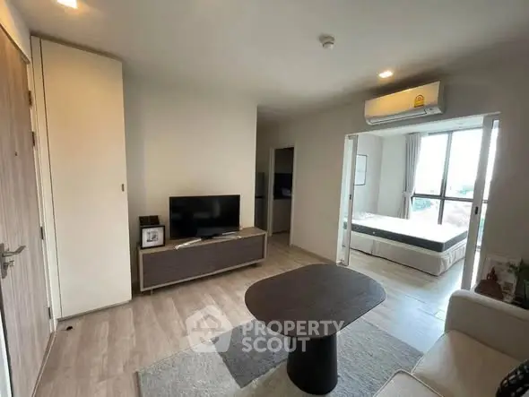 Modern living room with open view to bedroom, featuring sleek furniture and natural light.