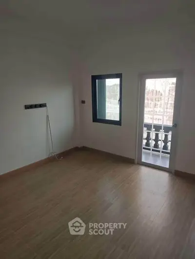 Spacious empty room with wooden flooring and balcony access, ideal for customization.