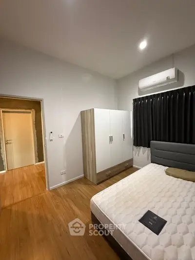 Modern bedroom with wooden flooring, white wardrobe, and air conditioning unit.