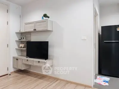 Modern living room with sleek TV setup and stylish shelving, adjacent to a kitchen area with a black fridge.