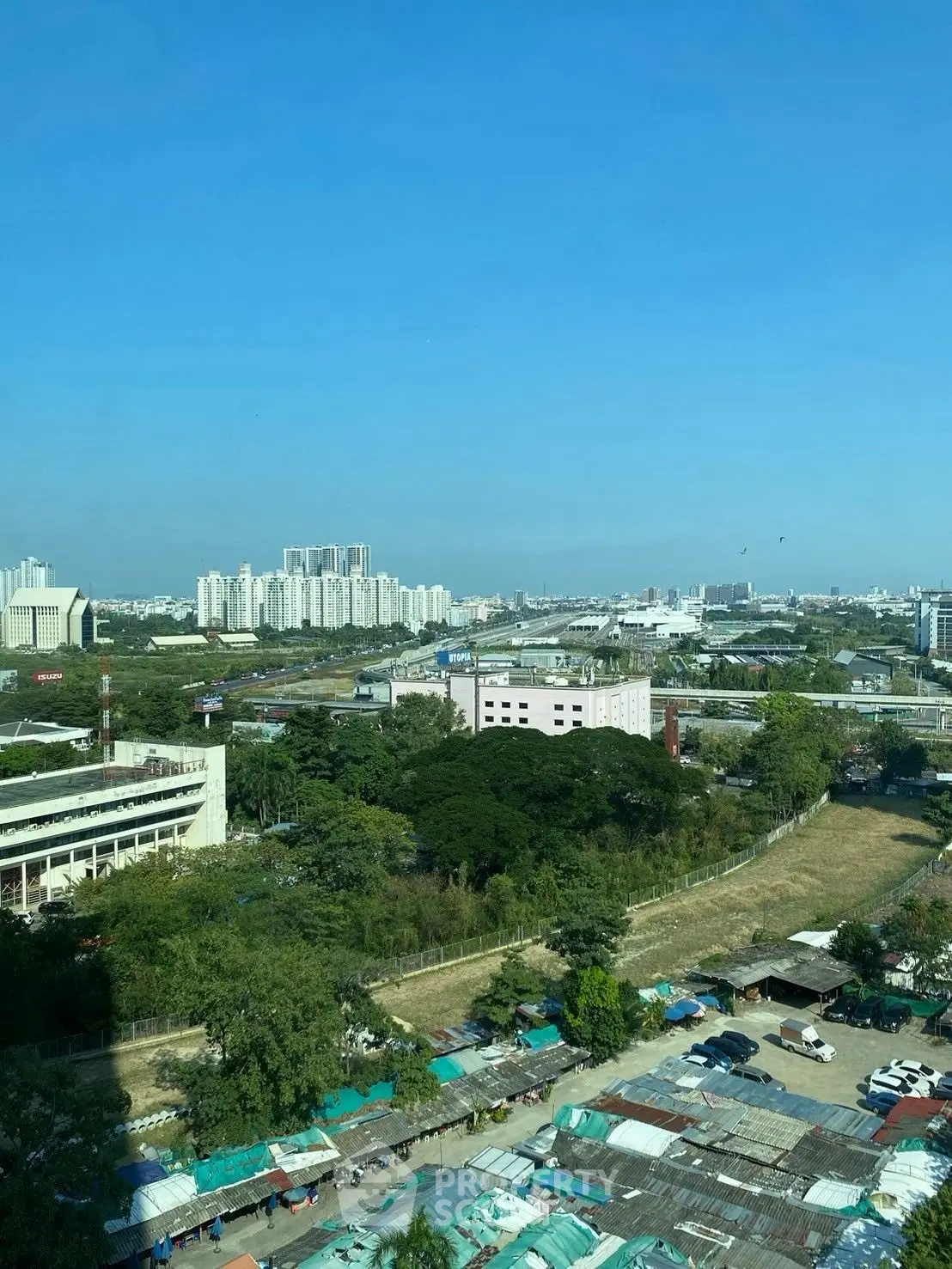 Stunning cityscape view from high-rise building with clear blue sky, showcasing urban development and greenery.