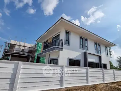 Modern two-story house with balcony and white fence under blue sky