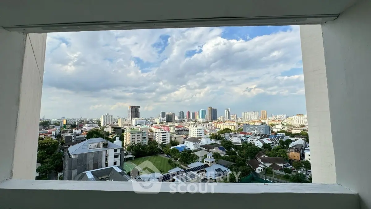 Stunning cityscape view from a high-rise building window, showcasing urban skyline and lush greenery.