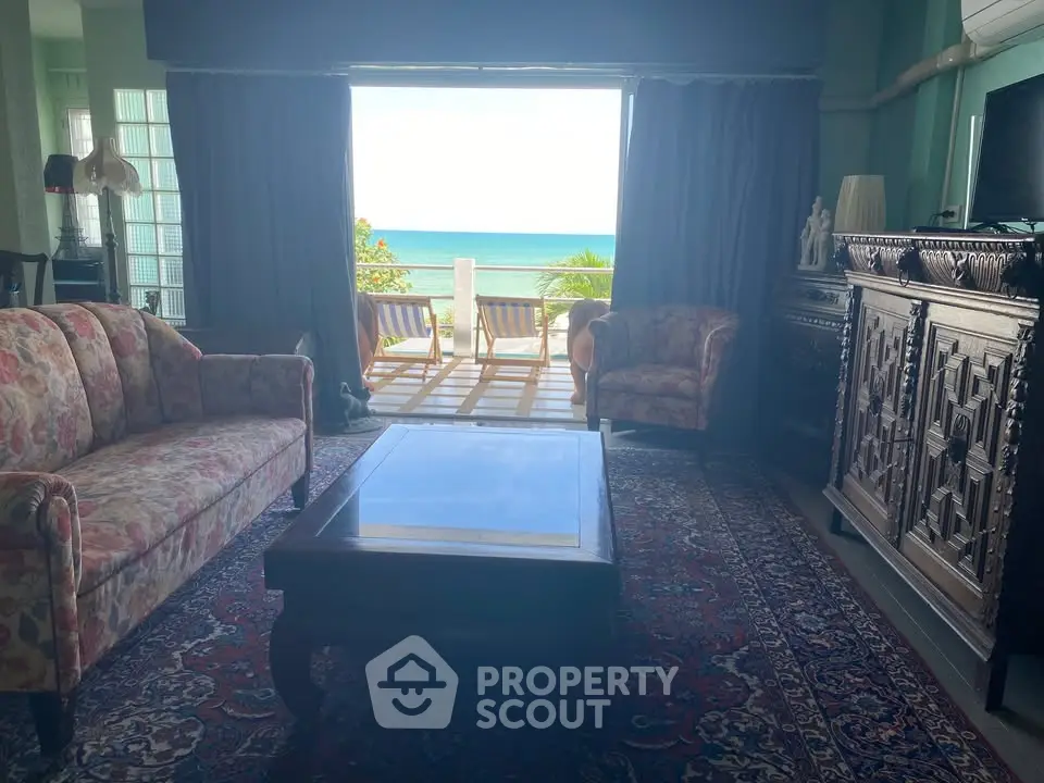 Luxurious living room with ocean view, elegant furniture, and large glass doors opening to a stunning seaside balcony.