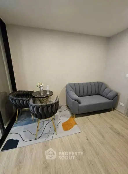 Modern living room with stylish gray sofa and chic chairs on a patterned rug.