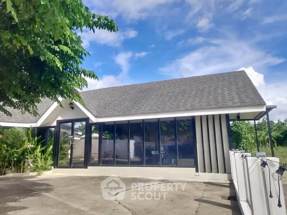 Modern single-story house with large glass windows and lush greenery, perfect for serene living.