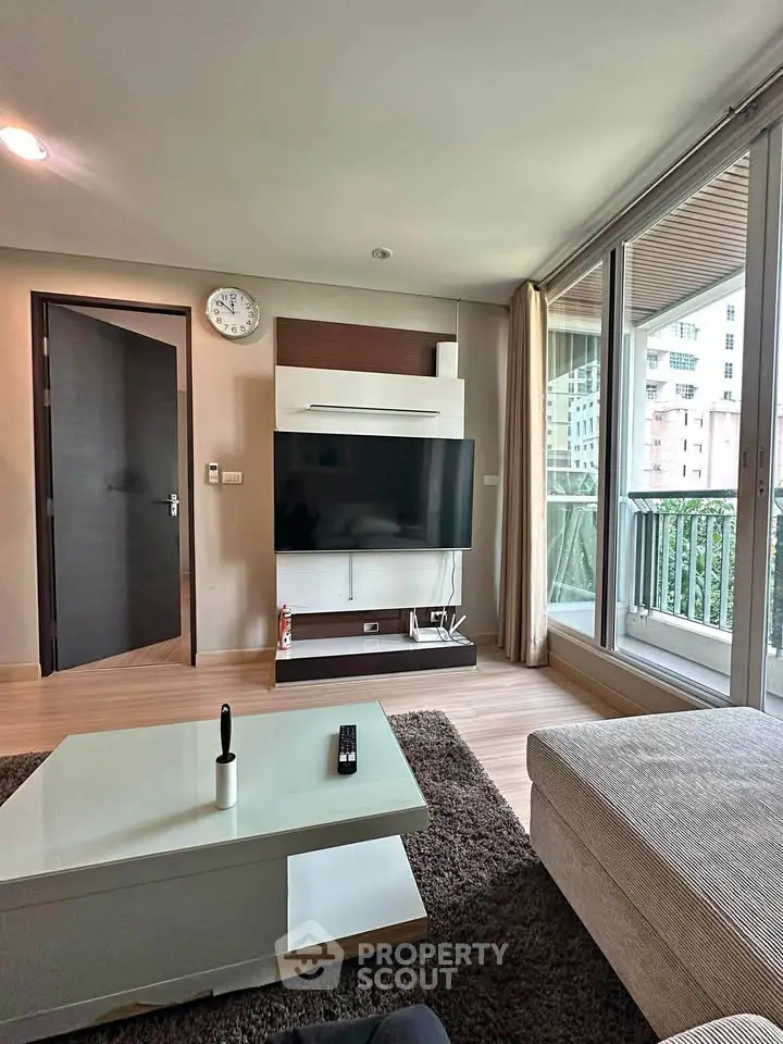 Modern living room with large TV, cozy seating, and balcony view in a stylish apartment.