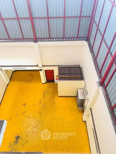 Spacious industrial warehouse with high ceilings and vibrant yellow flooring, ideal for storage or manufacturing.
