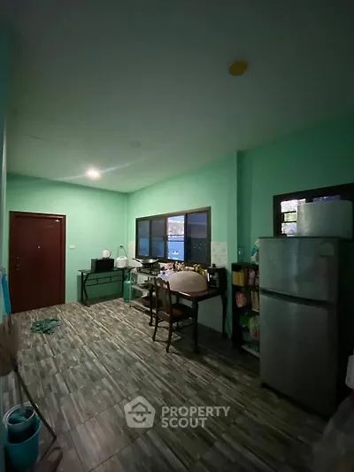 Cozy kitchen with green walls and dining area, featuring a fridge and ample natural light.