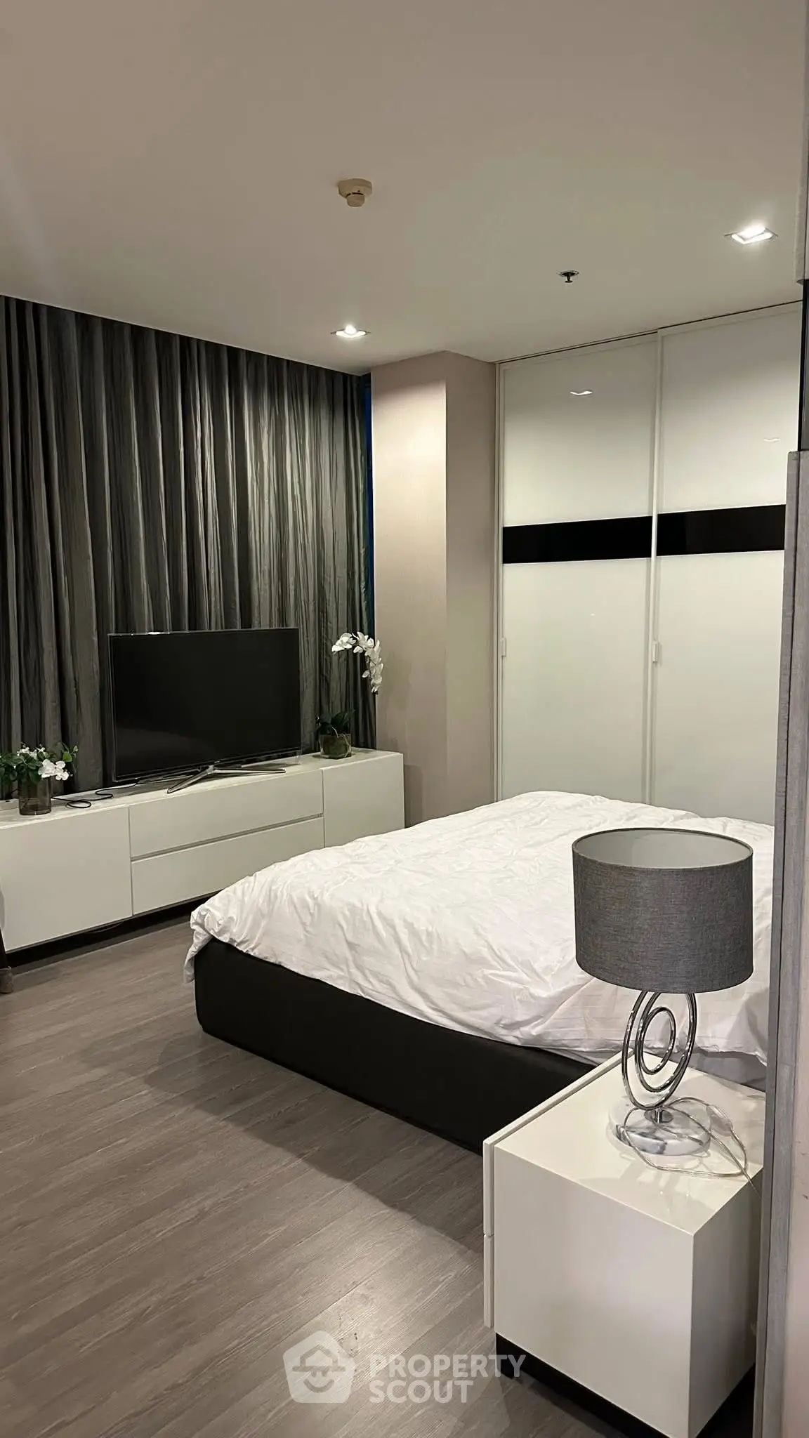 Modern bedroom with sleek design, featuring a cozy bed, stylish lamp, and elegant TV setup.